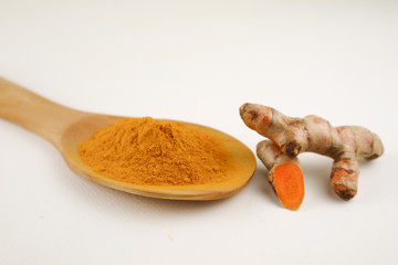 Turmeric powder in a spoon and turmeric root on a white background, used as a tonic for body and food ingredients.
