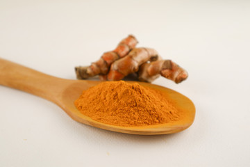Turmeric powder in a spoon and turmeric root on a white background, used as a tonic for body and food ingredients.
