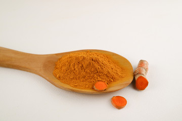 Turmeric powder in a spoon and turmeric root on a white background, used as a tonic for body and...