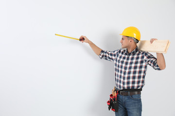 Handsome carpenter with wooden planks and measuring tape on light background. Space for text