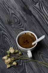 Coffee in a white cup. Nearby lies a flower of a dried beige rose. On brushed pine boards.