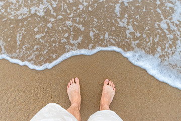 bare feet on a sandy beach with wave and foam