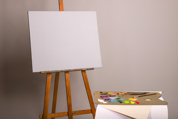 Oil painting. Easel and blank canvas. Palette with paints and brushes. Squeeze out oil paints on a palette and pieces of canvas. Clean canvas with copy space close up