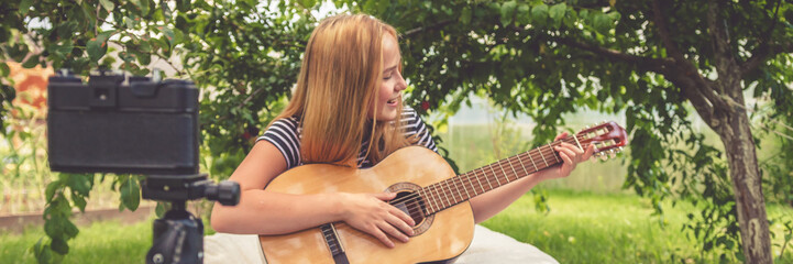 Teen girl shoots a blog on music and learning online guitar playing in nature in front of the camera, the idea of youth hobbies