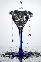 Full cocktail glass on blue thin and high leg with frozen water streams and flying water drops on...