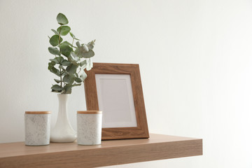 Wooden shelf with photo frame and decorative elements on light wall