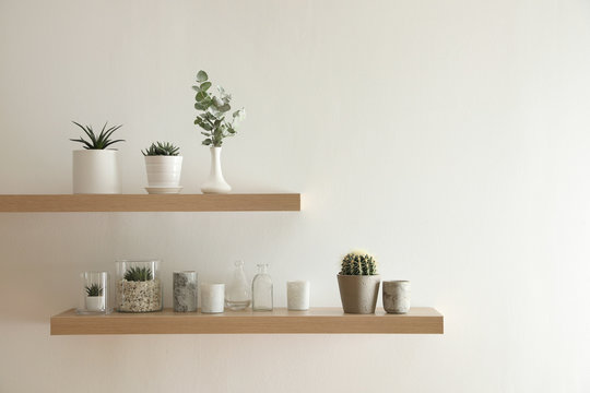 Wooden shelves with plants and decorative elements on light wall