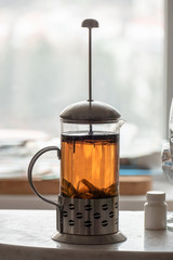  Glass jug with hot large-leaf tea on the marble table in home kitchen