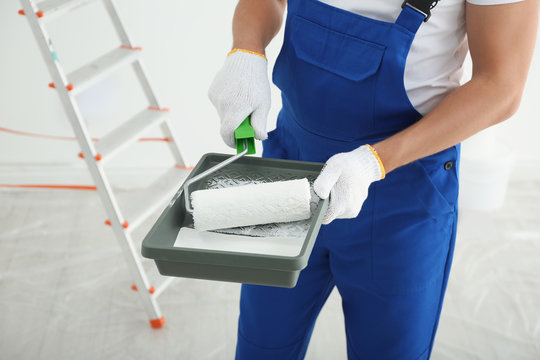 Man holding paint roller and tray in room, closeup