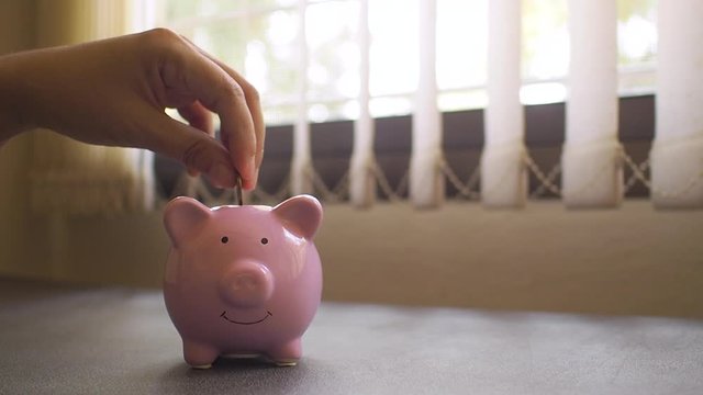 A business successful person is putting the coins in a pink piggy bank while working in the office. saving money is an investment for the future. Banking investment.