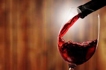Red wine being poured in wineglass on background