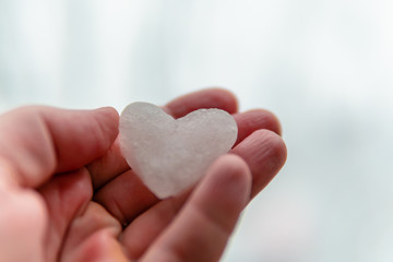 Fototapeta premium Snow heart melts in the hand. Snow in the shape of a heart on a palm on a background of a bright winter landscape. Ice in frosty weather. Love on Valentine's day concept