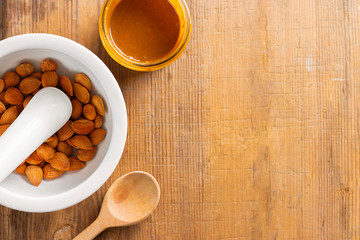 Glass jar with aprikot kernel butter, spoon, mortar with pestle with whole nuts on wooden background with copy space. Product is good for cardio vascular system, full of vitamims. Top view. Horizontal