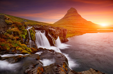 Colorful sunrise on Kirkjufellsfoss waterfall. Amazing morning scene near Kirkjufell volkano, Iceland, Europe. A famous tourist attraction near the city of Grundarfjordur. Travel concept background.