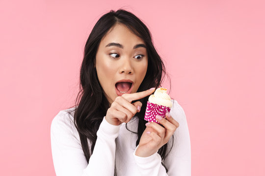 Image of young brunette asian woman smiling and holding cupcake