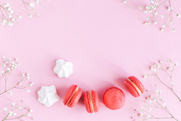 Pink macarons, white marshmallows and flowers on a pink pastel background.