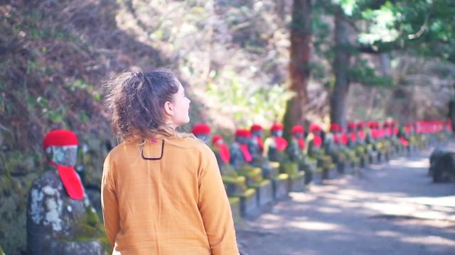 Slow motion of young woman back walking near row of Jizo statues in Kanmangafuchi Abyss in Tochigi prefecture in Nikko, Japan in early spring with moss