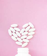 White pills in heart shape with bottle on pink background. Copy space for text