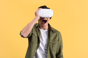 excited young man yelling while using virtual reality headset, isolated on yellow
