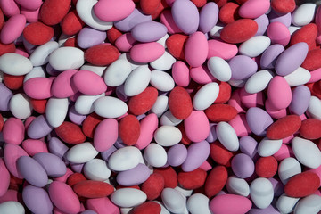A bunch of colorful chocolate dragees. Almond covered with chocolate and multicolored glaze. Red pink and purple sweets. Candy shop. Candy background.