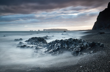 View on Dyrholaey Lighthouse. Famous tourist landscape with basalt rock formations Troll toes on black beach. Ocean waves flow around stones. Reynisdrangar, Vik, Iceland, Atlantic Ocean, Europe.