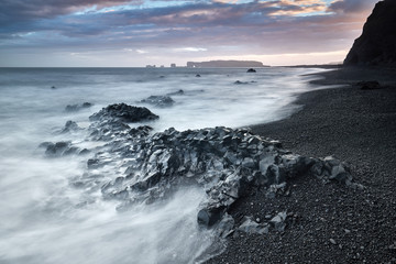 View on Dyrholaey Lighthouse. Famous tourist landscape with basalt rock formations Troll toes on black beach. Ocean waves flow around stones. Reynisdrangar, Vik, Iceland, Atlantic Ocean, Europe.