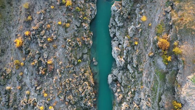 Rough rocky ground at the banks of a narrow stream. Cijevna (Cem) river in Montenegro. Vegetation of yellow bushes along the mountain river in autumn, in the afternoon sun. Aerial footage.