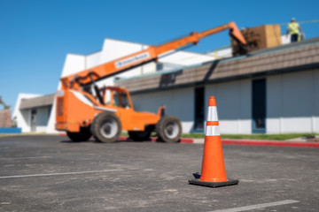 Orange traffic cone on asphalt parking lot near hydraulic forklift where a building roof is being...
