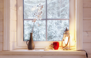 Festive lantern, red mug and heart on a wooden window sill in winter indoors.