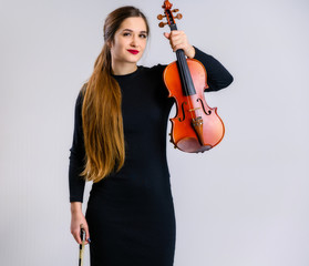 Portrait of a pretty brunette musician girl with a smile in a black dress on a white background holds a violin in her hands