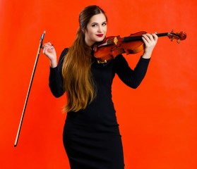 Portrait of a pretty brunette musician girl with a smile in a black dress on a red background holds...