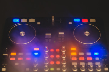 Dj sound mixer controller with knobs and sliders. audio mixing deck with turntables at dark with illuminated controls