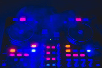 Dj sound mixer controller with knobs and sliders. audio mixing deck with turntables at dark with illuminated controls