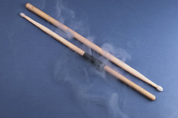 A pair of wooden drumsticks in the smoke on color background