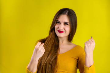 nice brunette girl with long hair with a smile in a yellow jacket rejoices on a yellow background, smiles and shows positive emotions