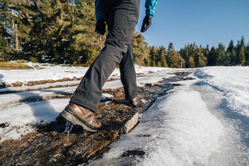 Trekking or hiking on a wet trail. Close up shot of hiking boots or shoes. Outdoor path with snow and water. Detail photo of outdoor hiking boots.