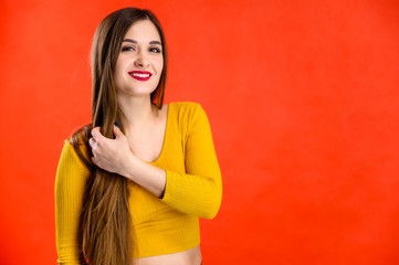 nice brunette girl with long hair with a smile in a yellow sweatshirt rejoices on a red background smiles and shows positive emotions