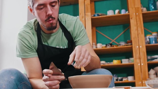 Man potter sculpting a pot out of clay auxiliary using scapula - polishing the sides with removing exes