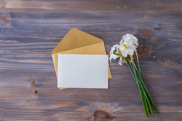 Mockup white greeting card and envelope with white daffodils on a wooden table
