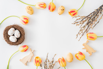 Flat lay easter composition with yellow tulips and eggs on a white background