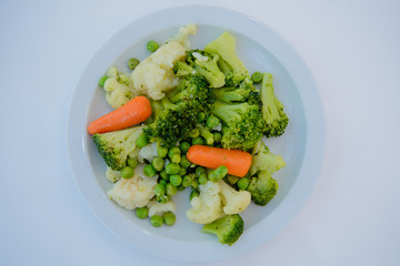 Cooked salad, carrots, peas, Brussels sprouts on a white plate