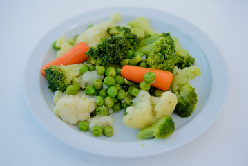 Cooked salad, carrots, peas, Brussels sprouts on a white plate