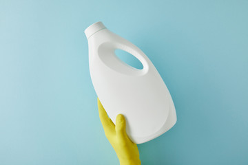 cropped view of housekeeper in rubber glove holding bottle with cleaning product on blue