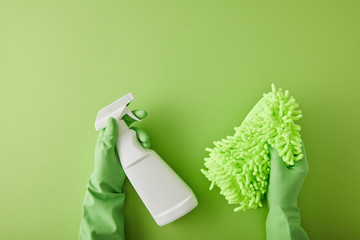 top view of housekeeper in rubber gloves holding spray bottle and rag on green