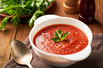 Tomato soup in a white bowl with parsley on a wooden table