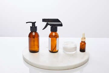Dispenser bottles of oil and cosmetic cream on round stand isolated on grey