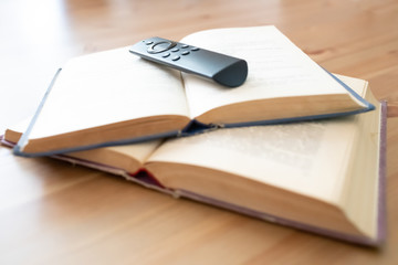 Close-up of two open books, one on top of the other, with a television remote control on the top, all set on a table with selective focus.