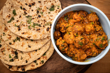 Potato curry (Kashmiri dum aloo) with chapatti (roti) served on wooden dining table.