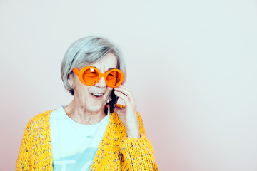 a surprised smiling elderly woman wearing orange sunglasses speaking on the mobile phone - forever...