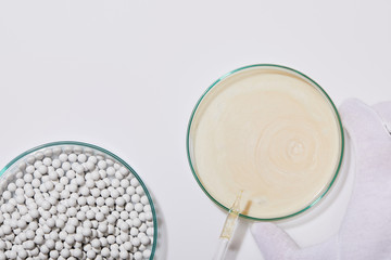Cropped view of person holding laboratory glassware with sample of cosmetic cream and ampoule next to decorative beads on grey background